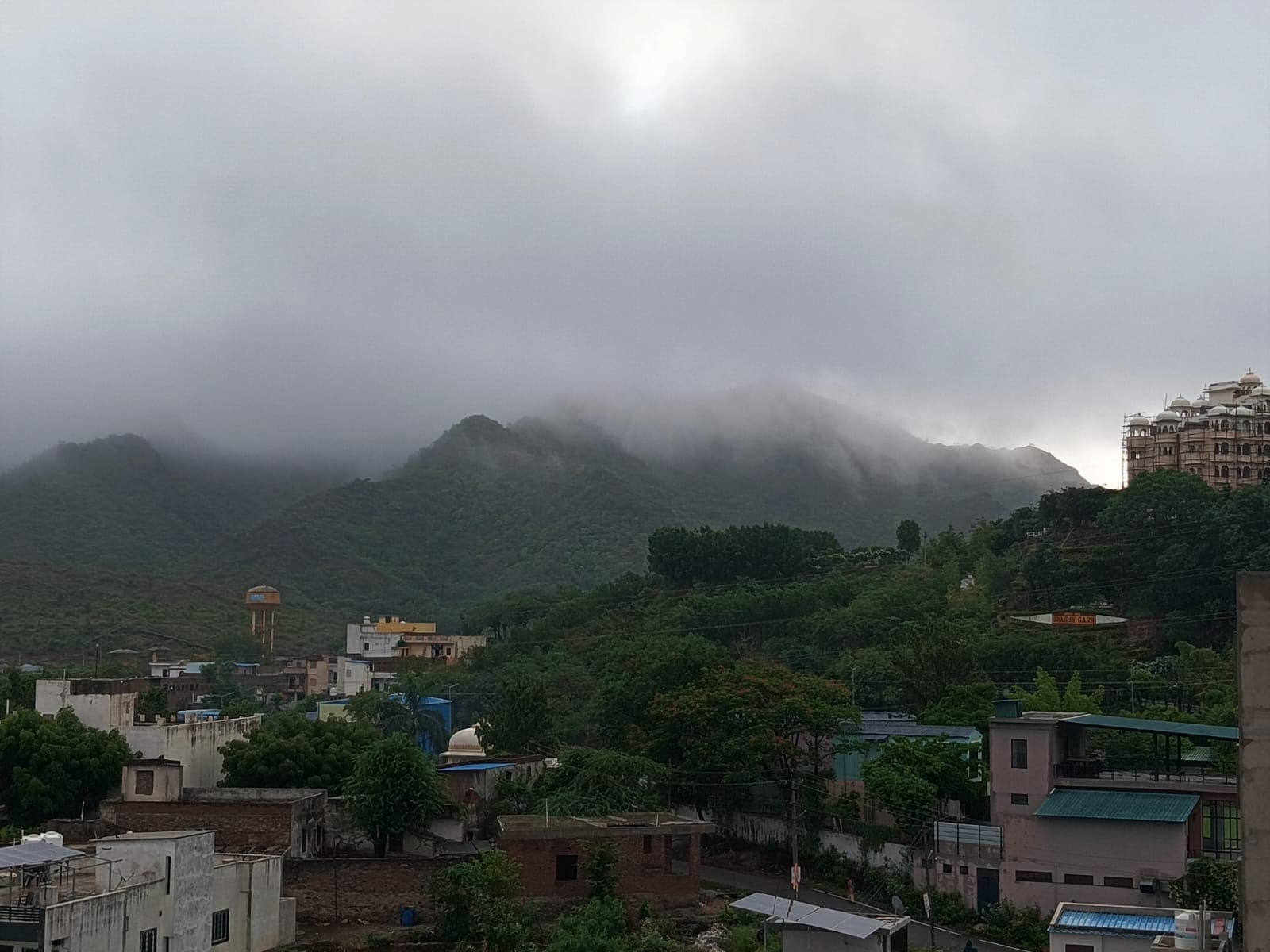 Monsoon cloud settling on the green Aravalli hills above the rooftops of Sukher