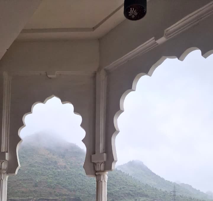 White cusped arches framing a hill wrapped in monsoon cloud