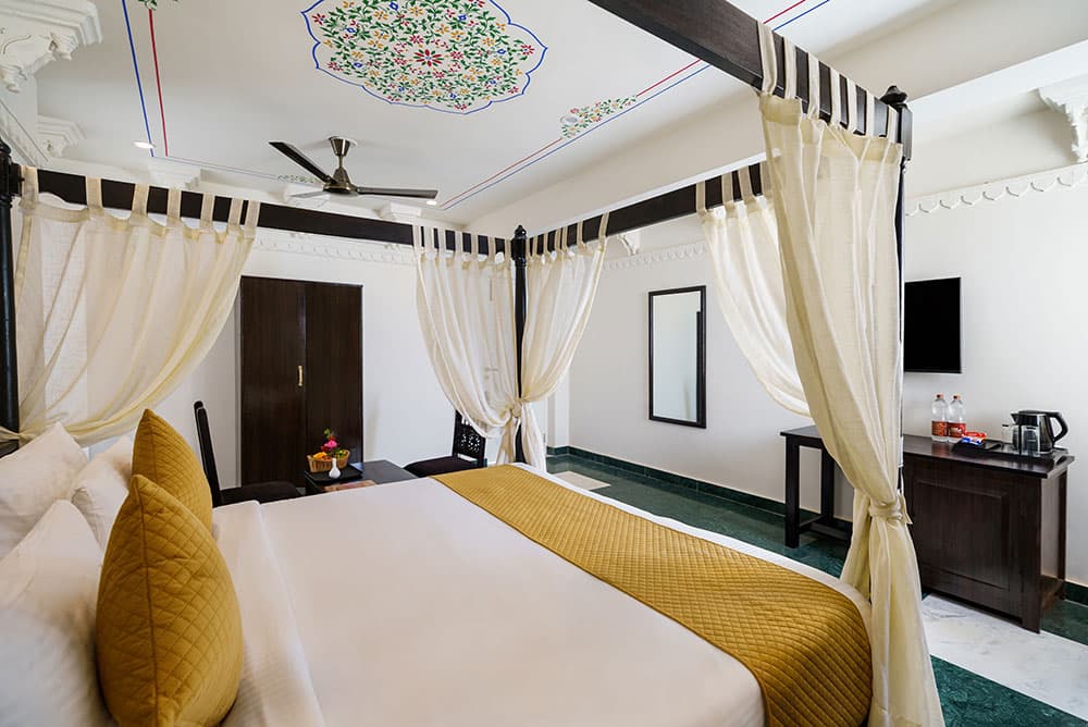 Guest room with a canopy bed, mustard-gold cushions and a green marble floor