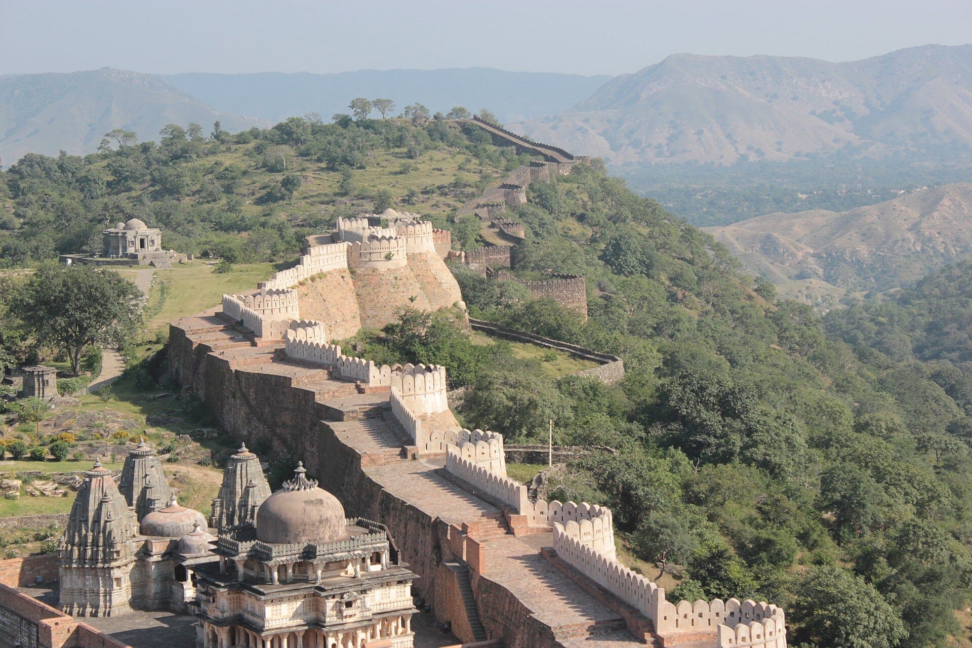 Kumbhalgarh Fort’s battlemented wall running along a green ridge, with temples below and hills beyond