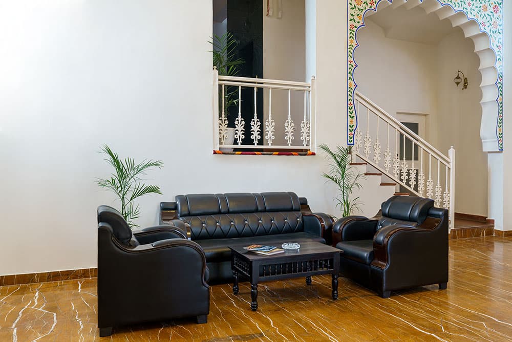Double-height lobby lounge with leather sofas, potted palms and a white staircase