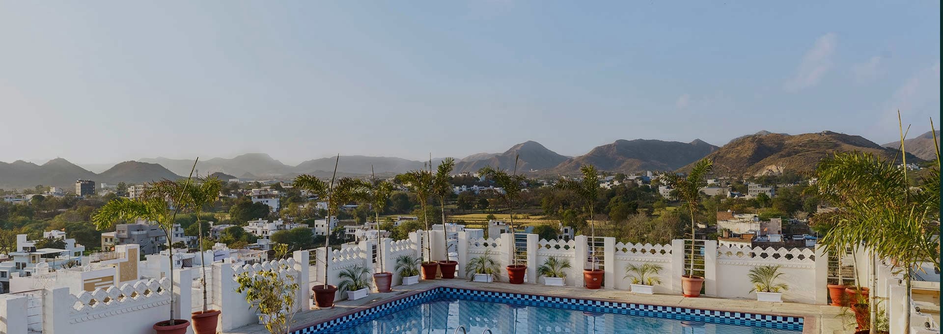 The rooftop pool terrace with its white scalloped parapet, palms and a view across Sukher to the Aravalli hills