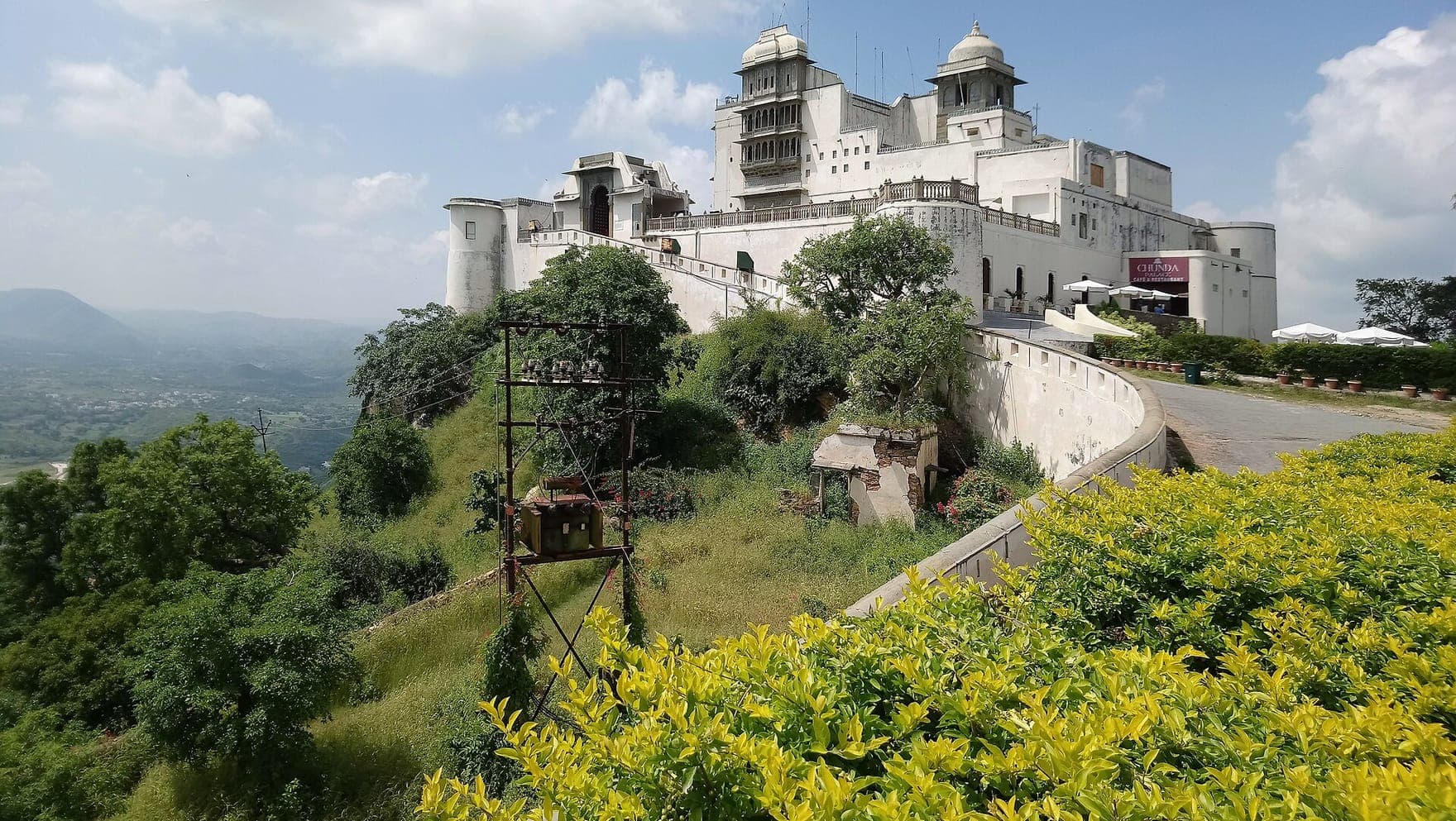 The white Sajjangarh Monsoon Palace on its green hilltop above Udaipur, under a cloudy sky