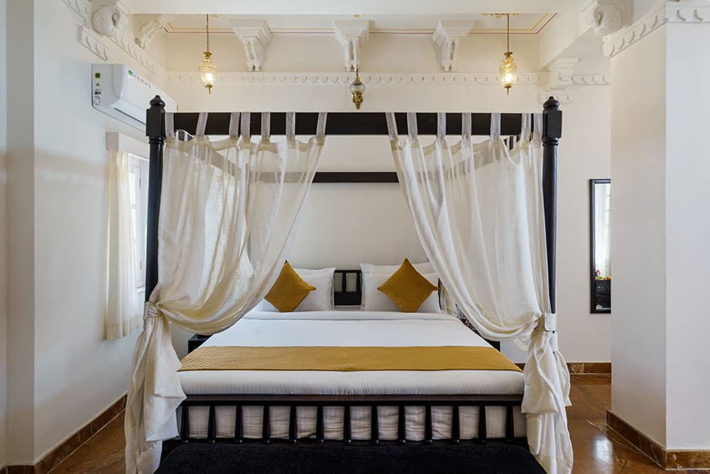 Four-poster bed in the Super Deluxe Room framed by sheer white curtains and gold cushions