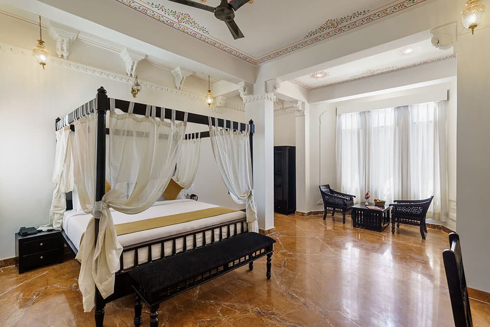 Spacious Super Deluxe Room with a four-poster bed, a carved bench and a seating area by the windows