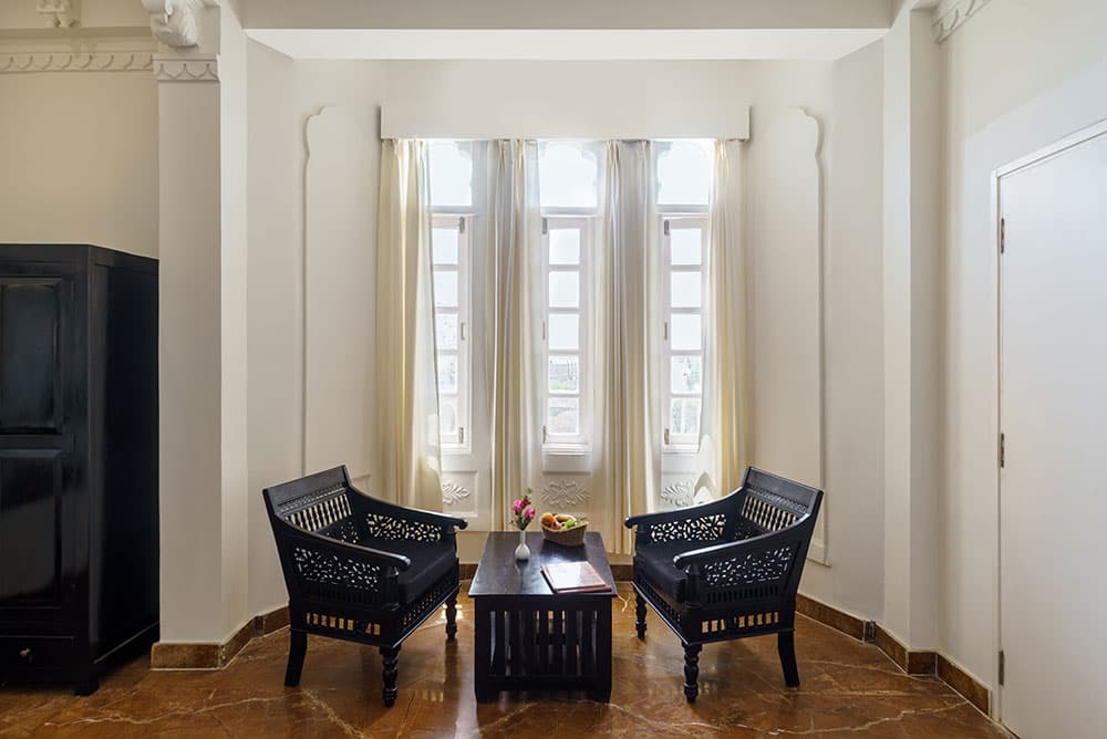Seating corner in the Super Deluxe Room with two carved wooden armchairs beneath tall windows
