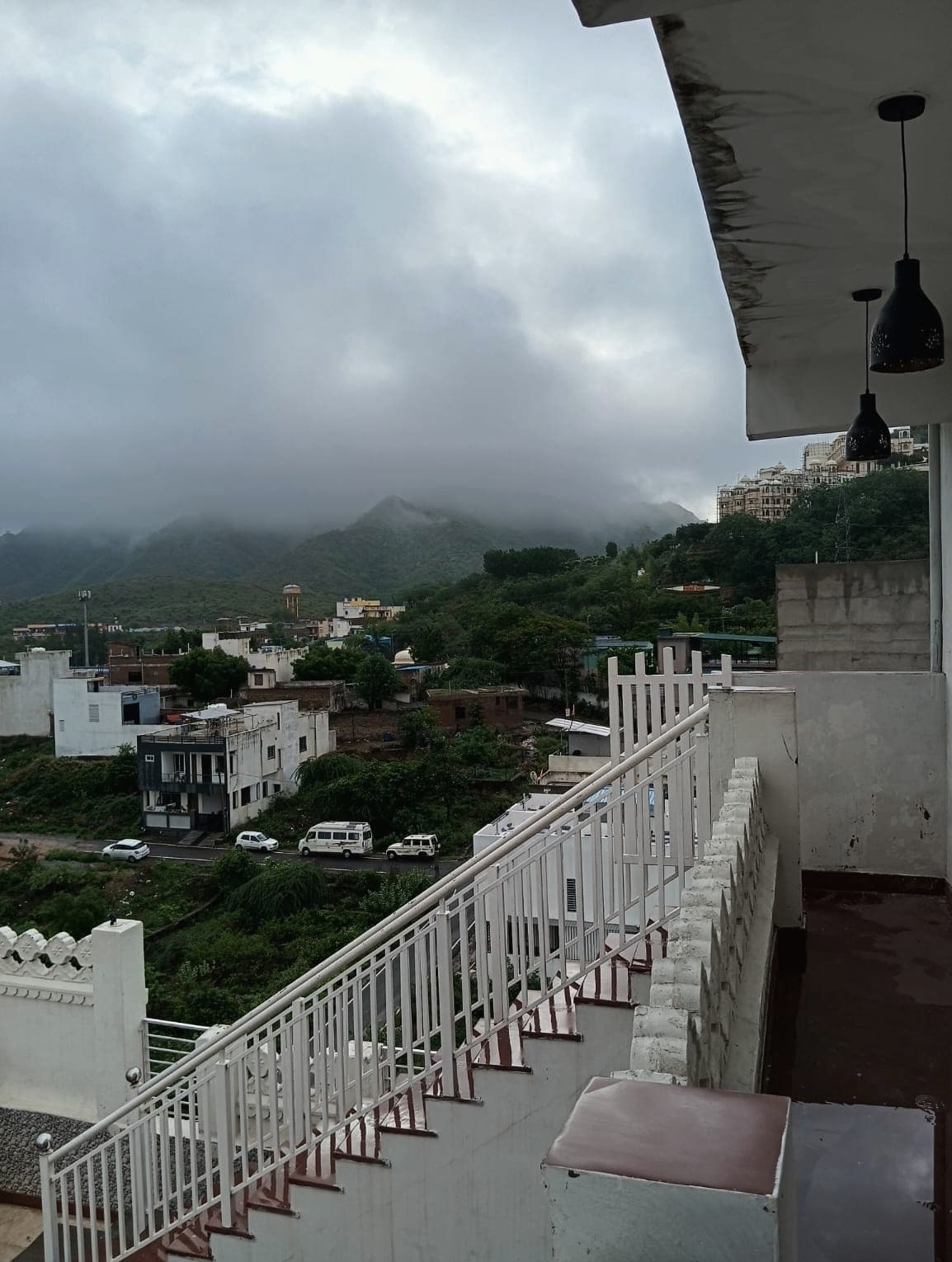 A white terrace stair and scalloped parapet looking out over Sukher to hills under heavy monsoon cloud