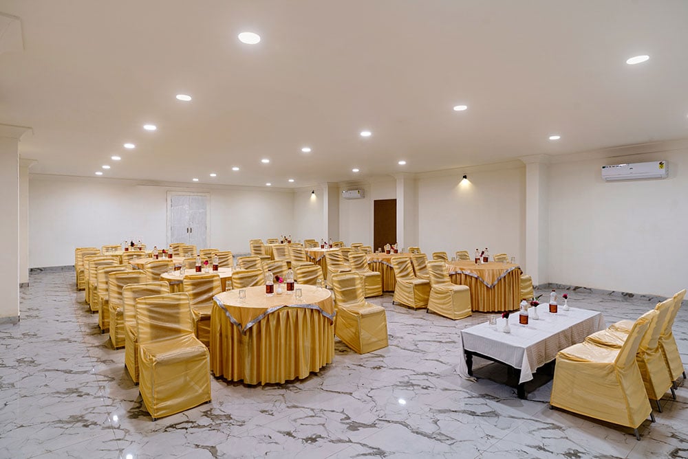 Banquet hall with gold-draped round tables and chair covers on a white marble floor