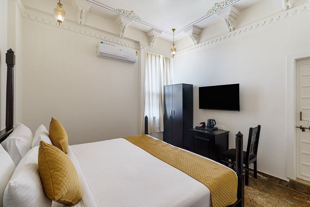 Deluxe Room with a white bed, mustard-gold runner and cushions, a dark-wood wardrobe and a wall-mounted TV