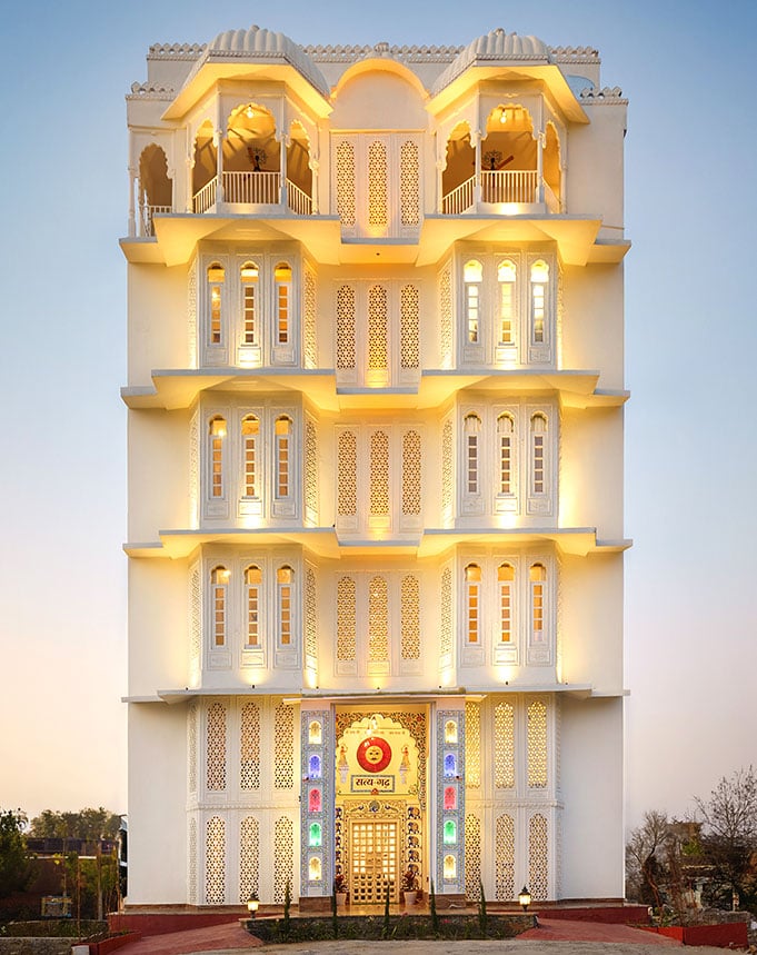The white façade of Hotel Rudra Kripa at dusk, its jharokha balconies lit in warm gold