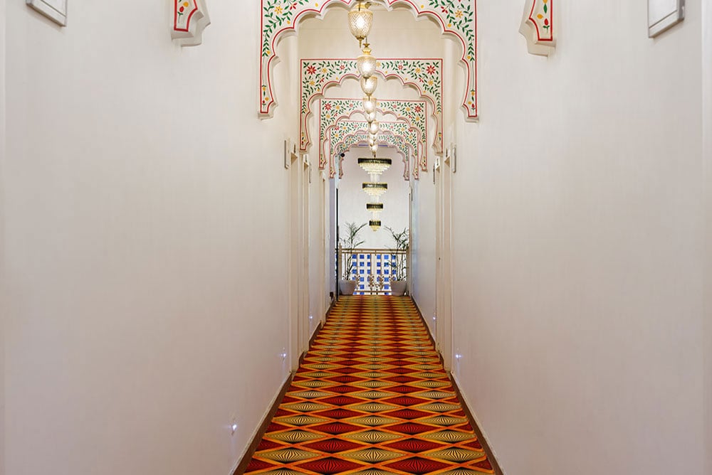 Corridor framed by painted Rajasthani arches over a red and gold patterned runner